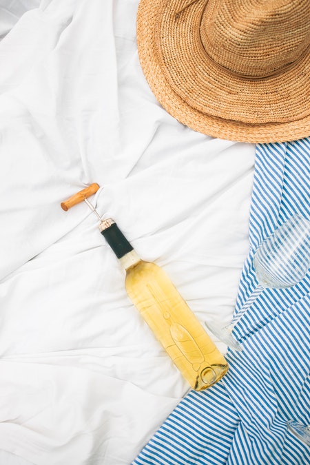 bouteille de vin blanc sur un drap blanc avec chapeau de paille et serviette a rayures bleues et blanches